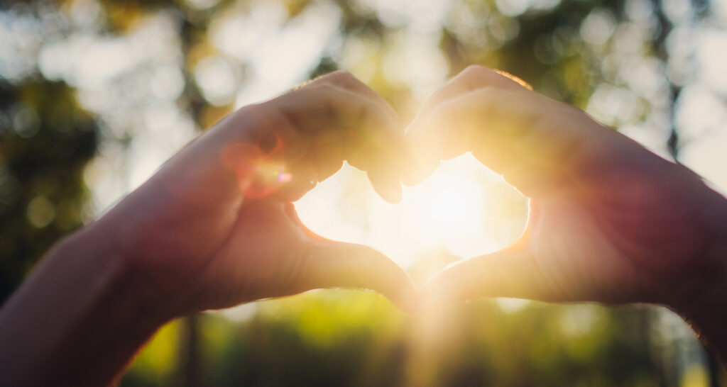 Closeup image of sunlight shining through heart hands sign with nature background